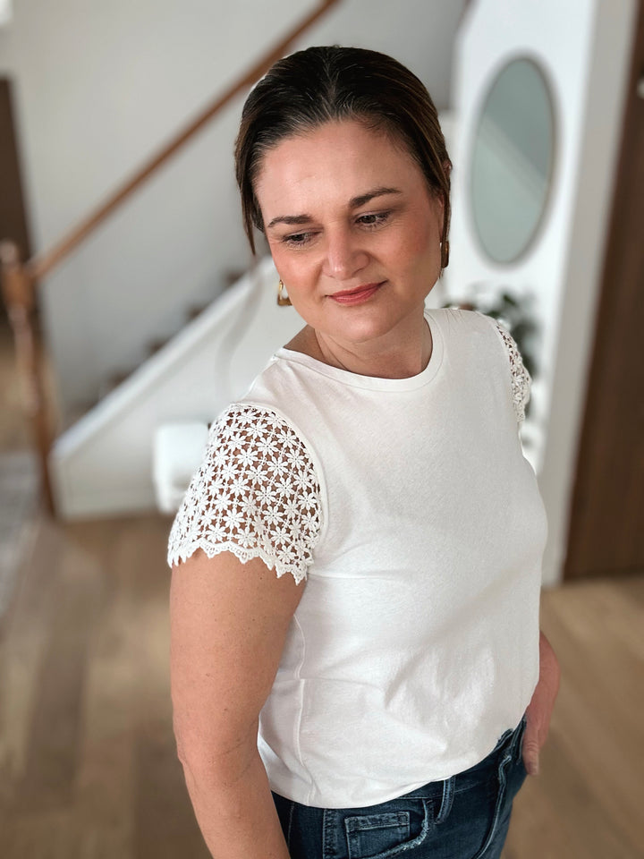 Woman wearing a white blouse with lace sleeves in an indoor setting