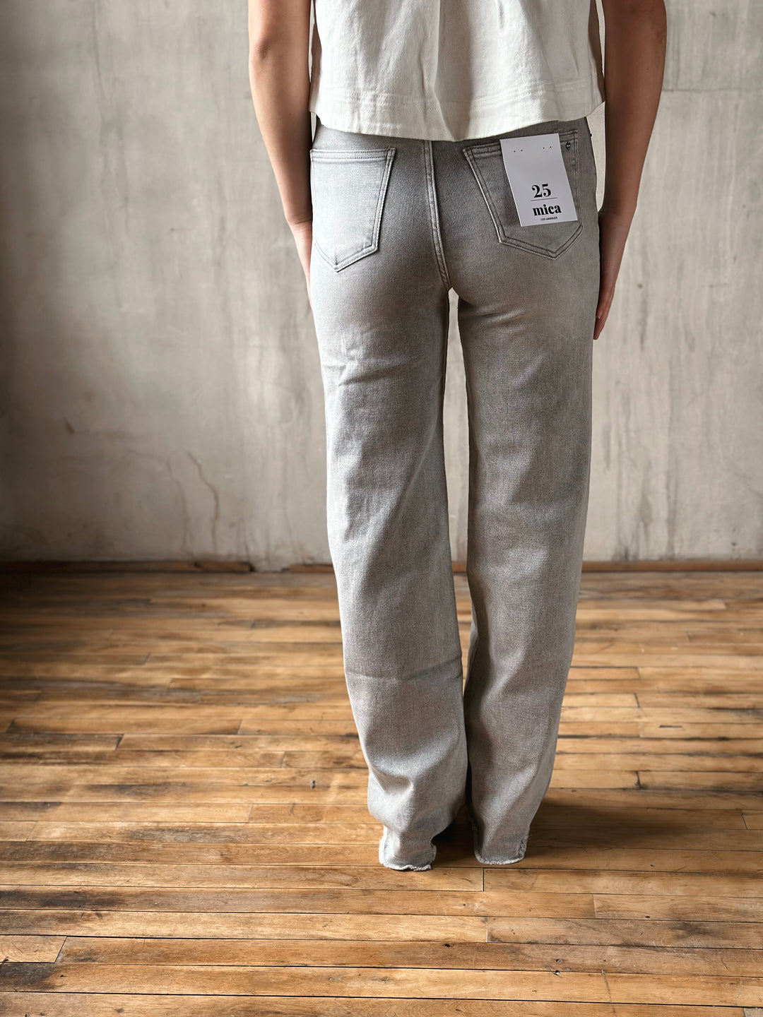 Person wearing gray jeans and a white shirt against a plain wall.