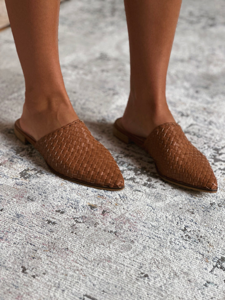 Brown woven shoes worn on a textured floor.