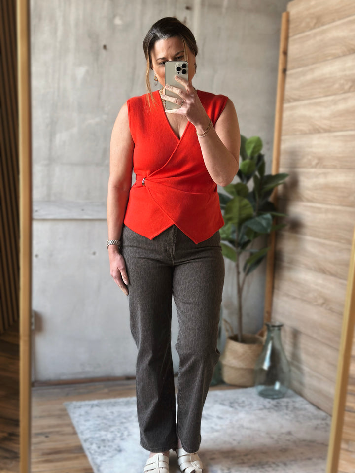 Person taking a mirror selfie wearing a red top and gray pants in a room with wooden walls and a plant.