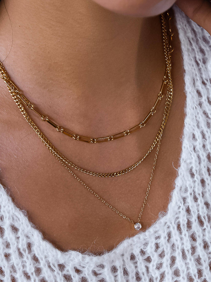 Close-up of a person wearing gold chain necklaces with a white lace garment.