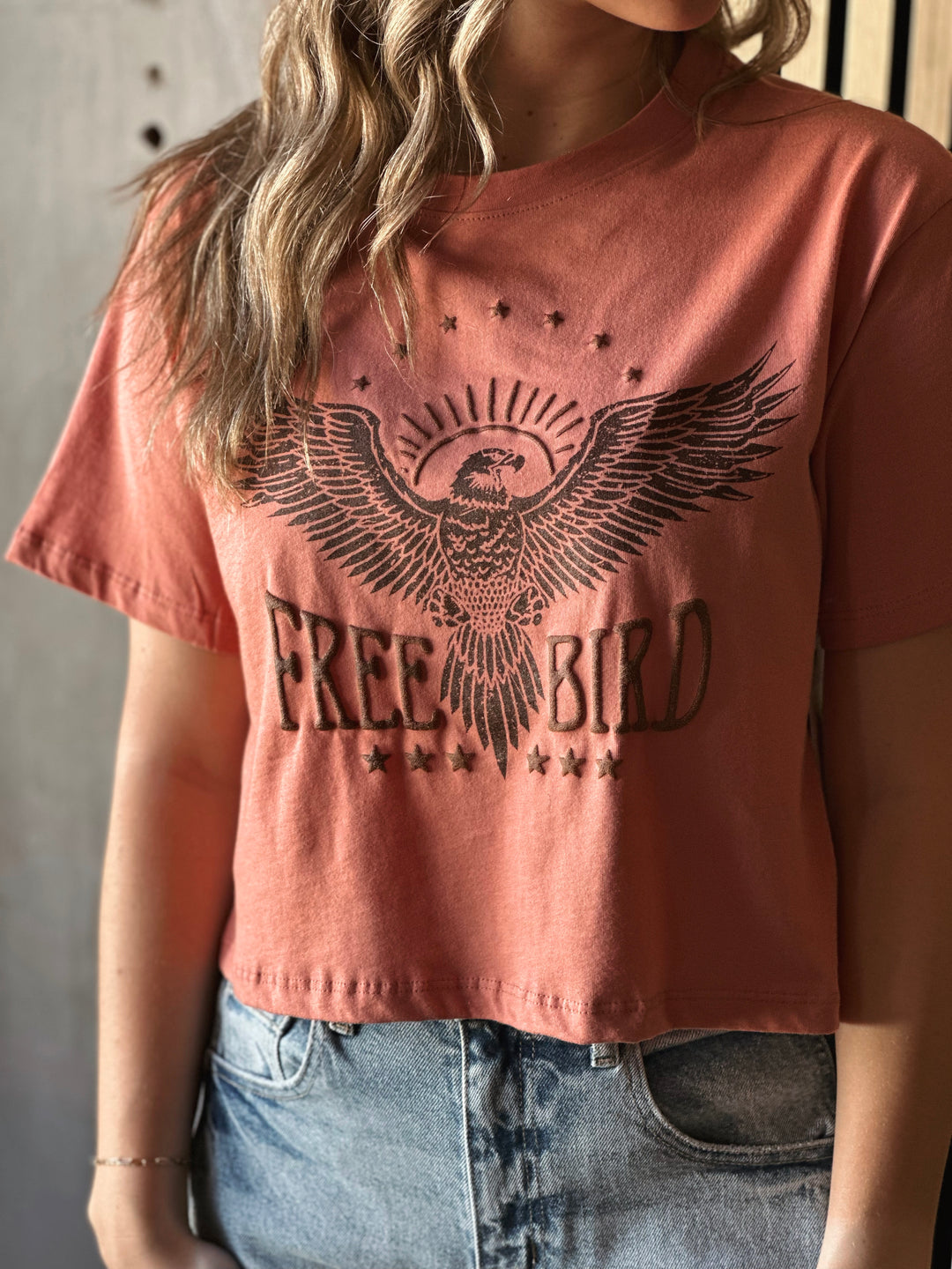 Front view of model wearing a mauve shirt with Free Bird graphic tee with puff print design