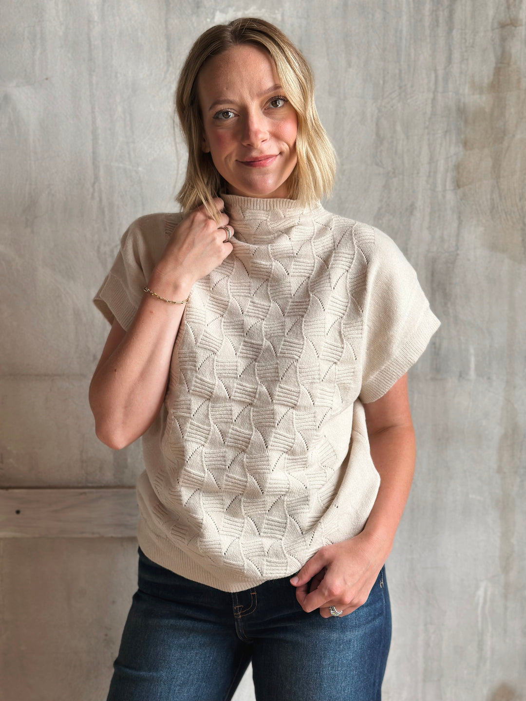 Woman wearing a beige knitted poncho against a gray concrete wall