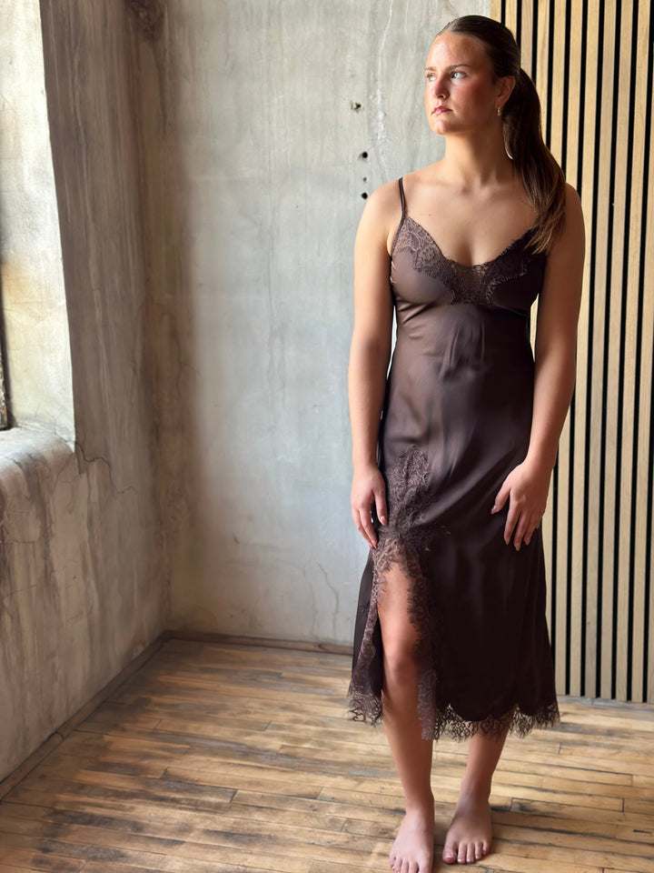 Woman wearing a chocolate brown satin slip midi dress with lace trim, side view