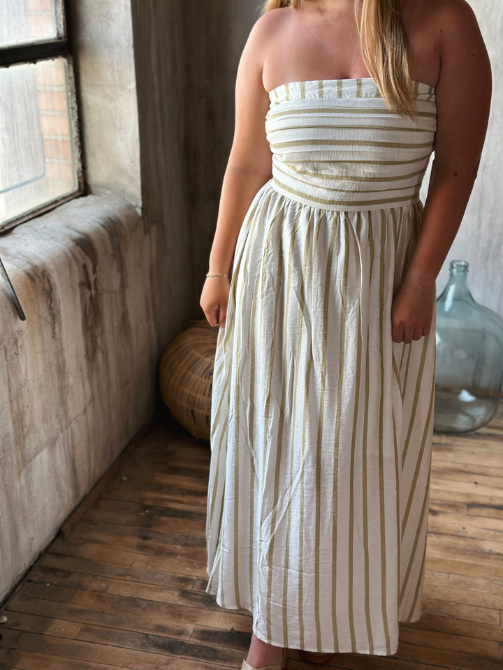 Woman wearing a strapless, white dress with thin beige stripes in a room with wooden floor and large window.