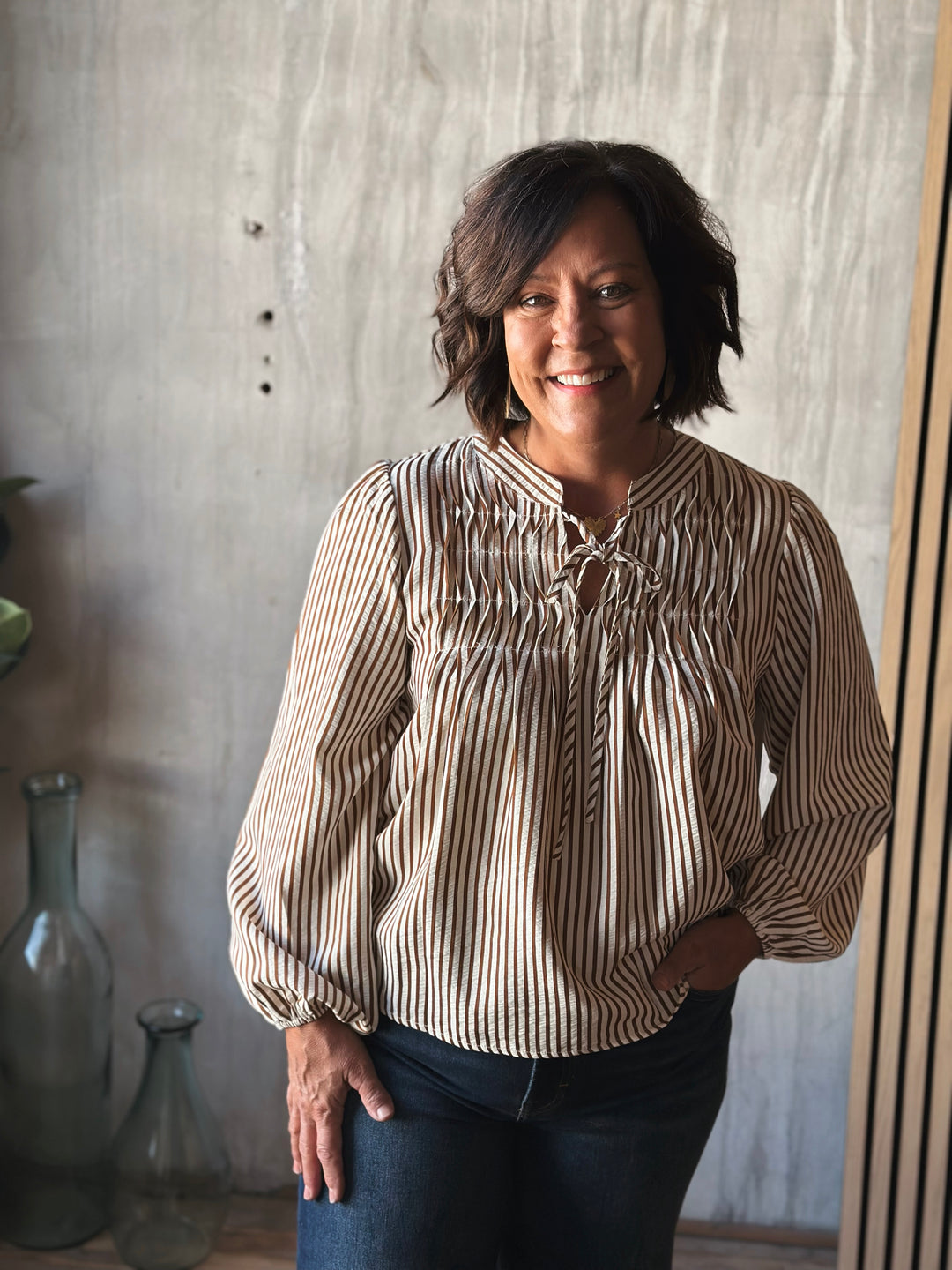 Woman wearing a striped blouse standing against a textured wall.