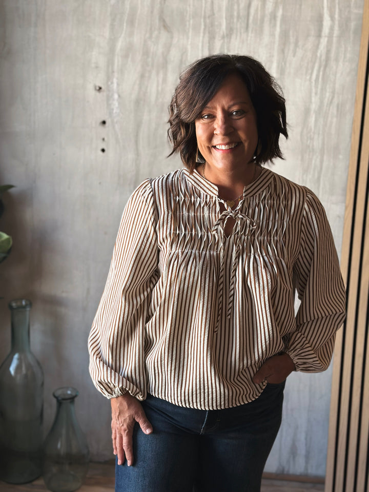 Woman wearing a striped blouse standing against a textured wall.