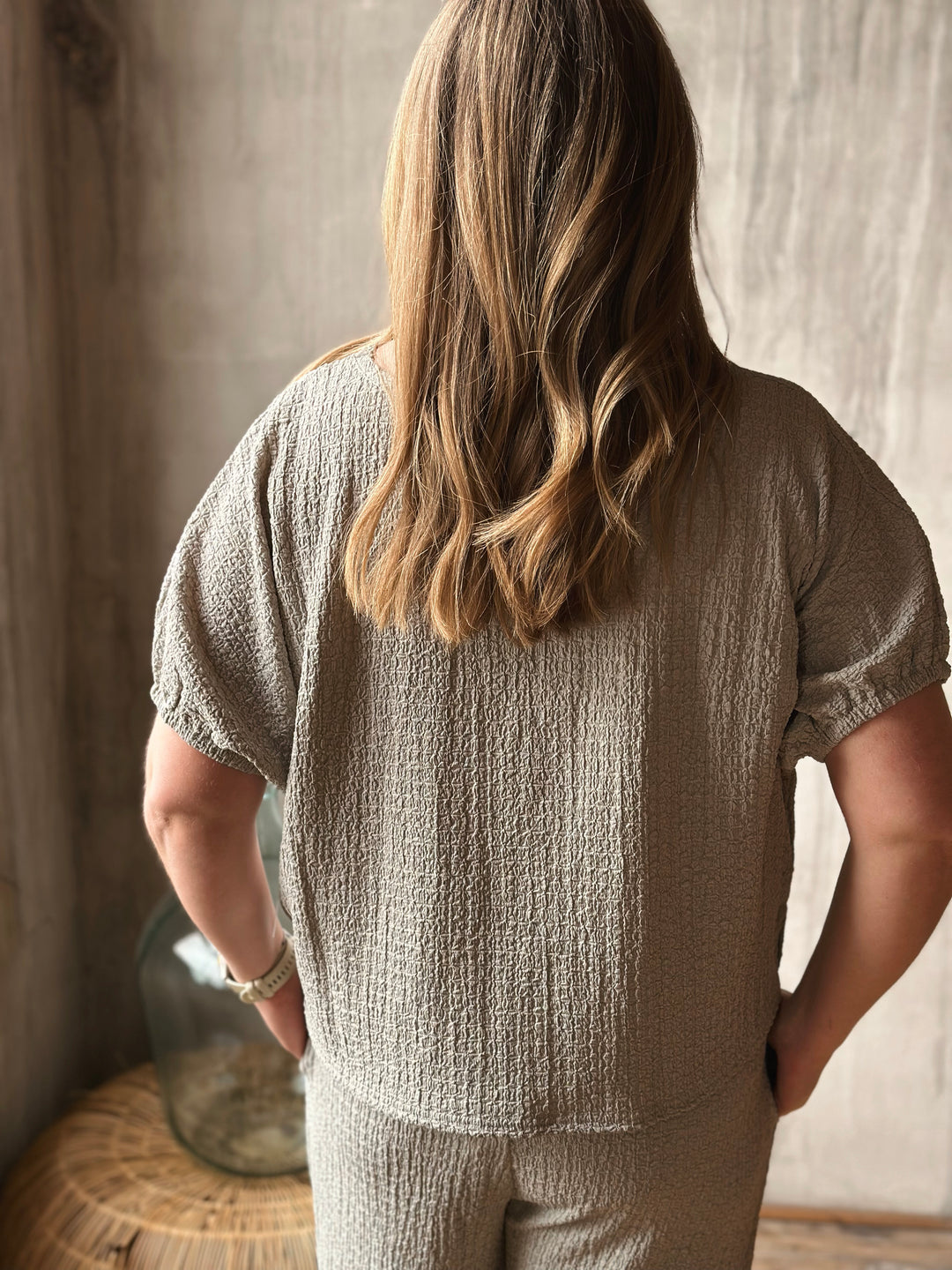 A person wearing a textured sage outfit standing in a softly lit room.