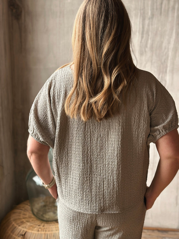 A person wearing a textured sage outfit standing in a softly lit room.