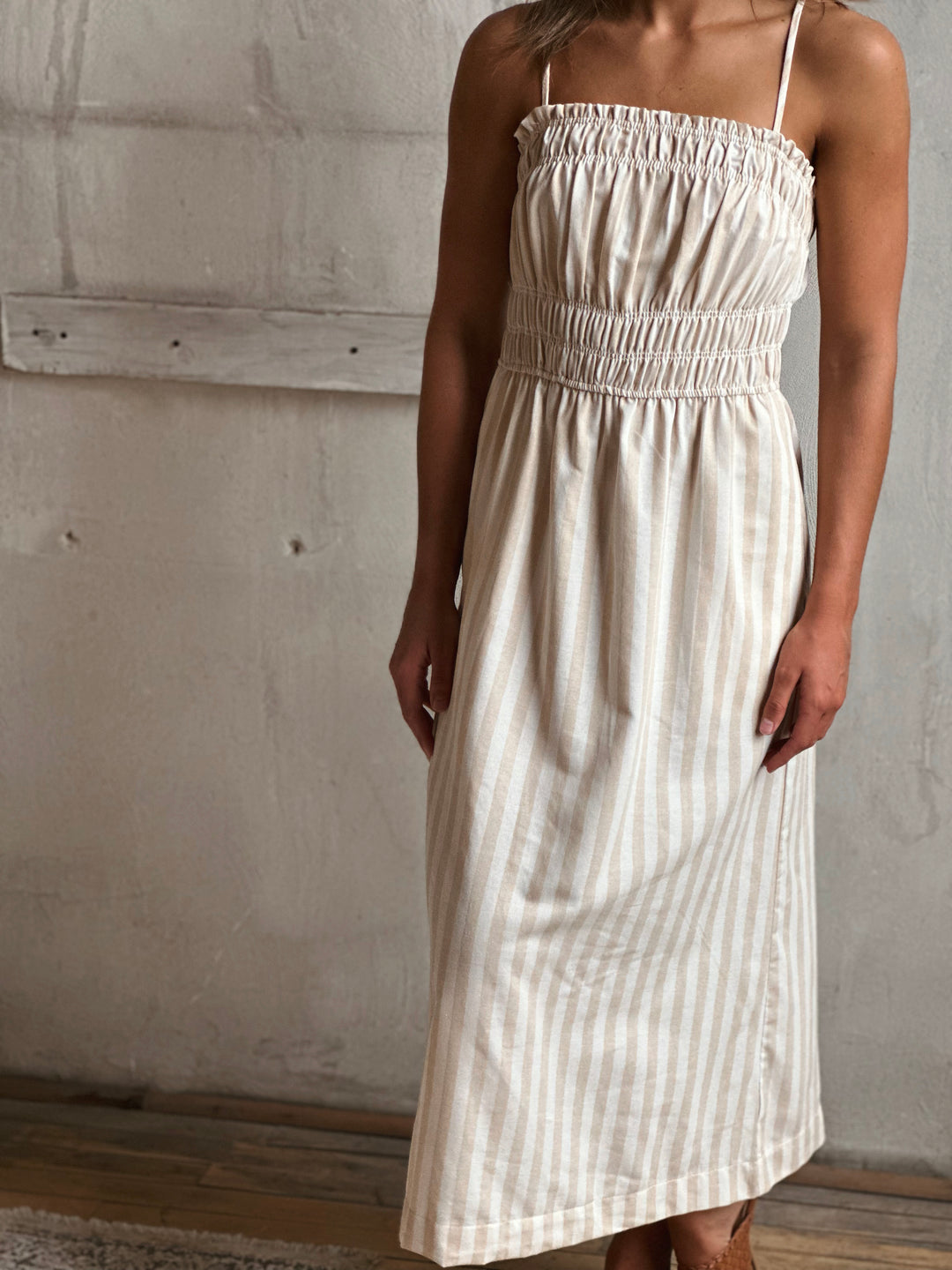 Woman wearing a white and cream striped dress against a plain wall.