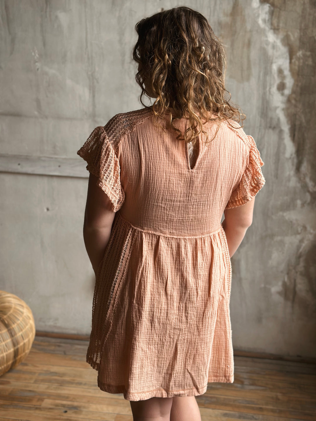 Woman wearing a peach colored dress standing against a textured wall.