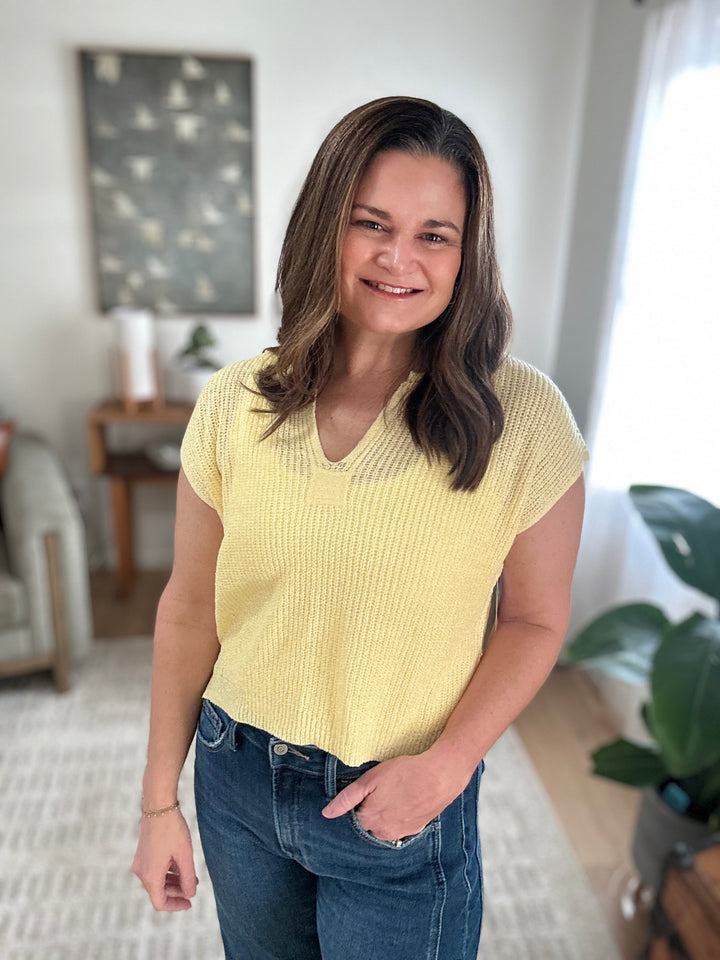 Woman wearing a yellow knitted sweater and blue jeans indoors.