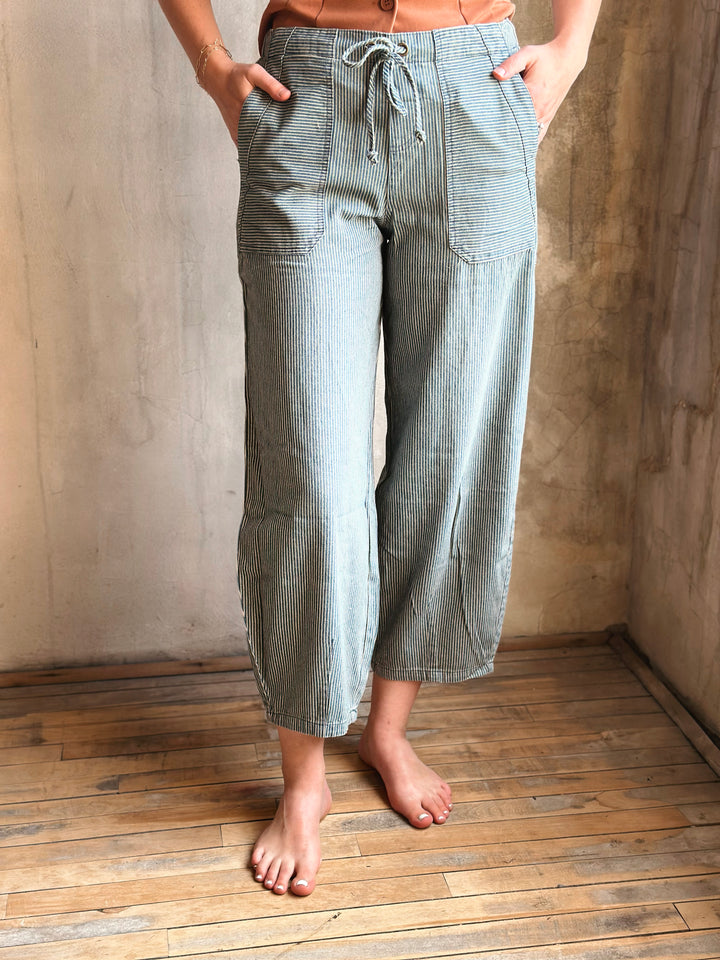 Person wearing light blue checkered pants standing on a wooden floor against a textured wall.