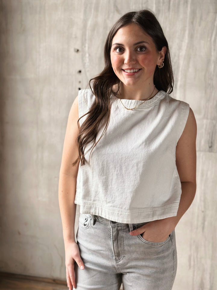 Woman wearing a white denim sleeveless top and gray pants against a neutral background