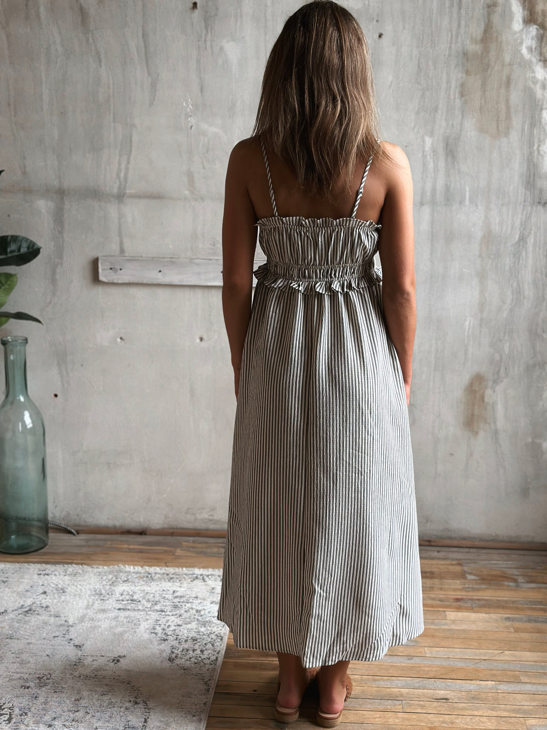 Woman wearing a white and gray striped dress standing in a room with a concrete wall and wooden floor.