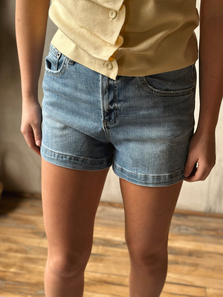 Person wearing light blue denim shorts and a yellow shirt indoors.
