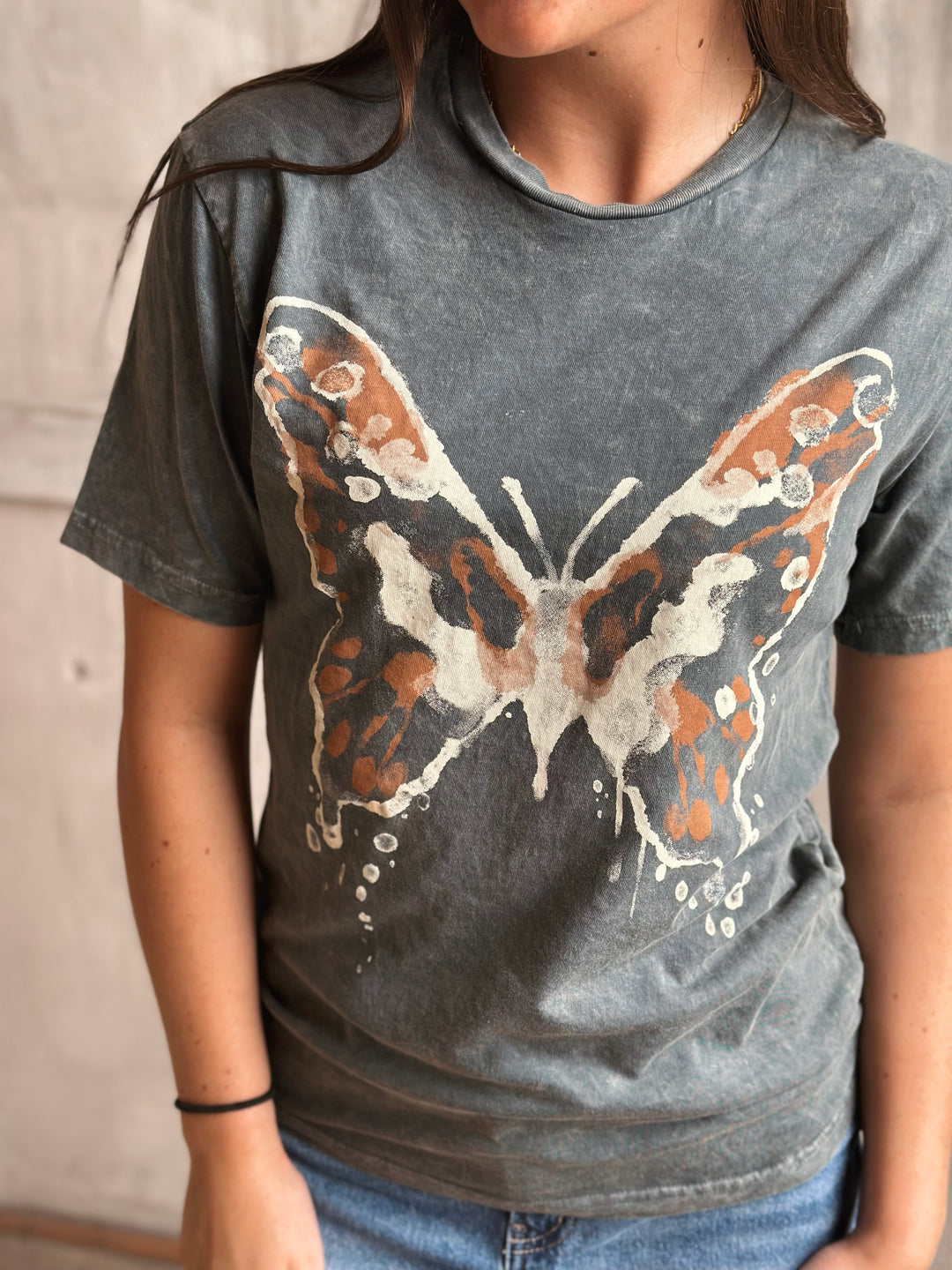 Person wearing a gray t-shirt with a butterfly design.