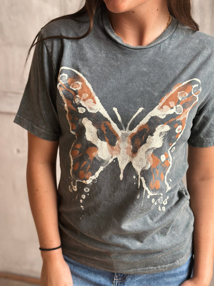 Person wearing a gray t-shirt with a butterfly design.