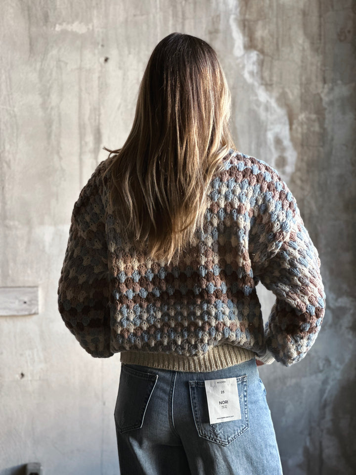 Person wearing a patterned sweater and jeans against a concrete wall.