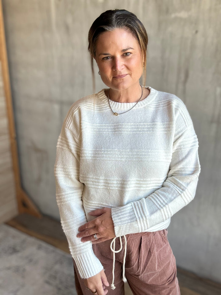 Woman wearing a cream textured-stripe crewneck sweater with mauve drawstring pants