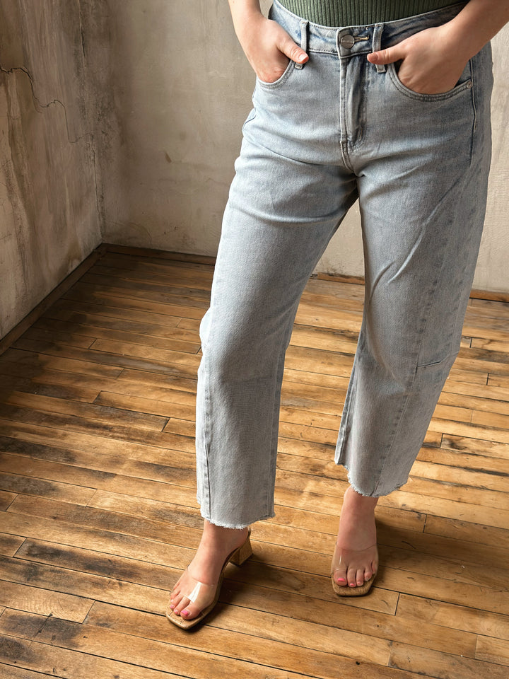 Person wearing light blue jeans standing on a wooden floor with a neutral wall background