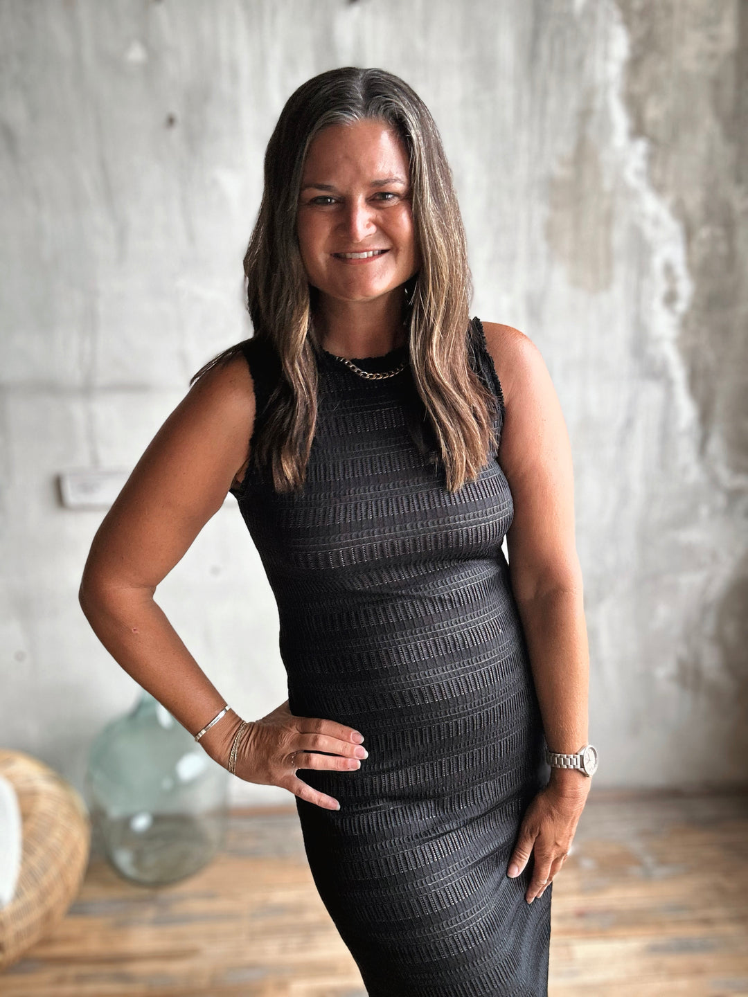 Woman in a black dress standing indoors with a neutral background