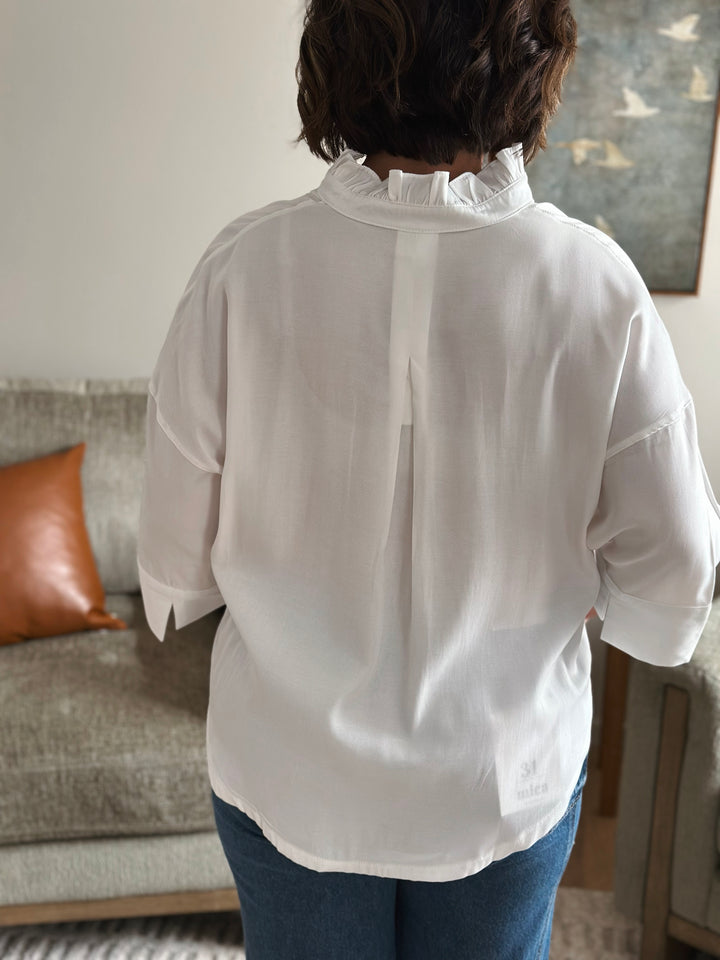 Person wearing a white blouse with ruffled collar in a living room setting