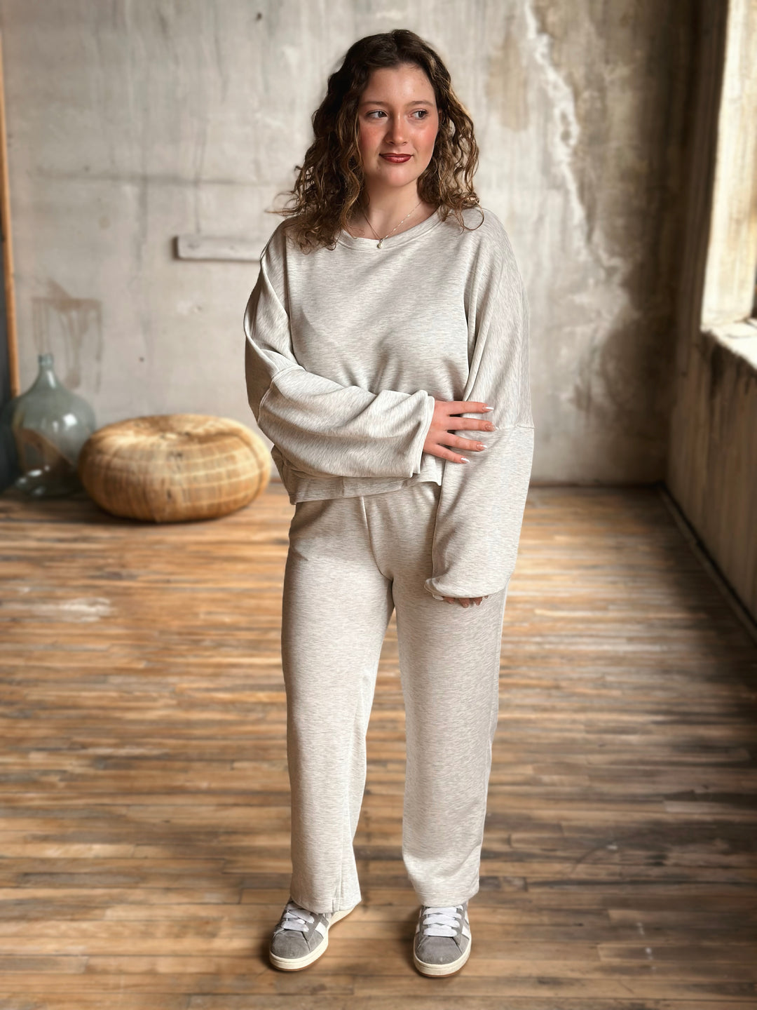 Woman wearing a light grey sweat set in a room with wooden floor and textured walls.