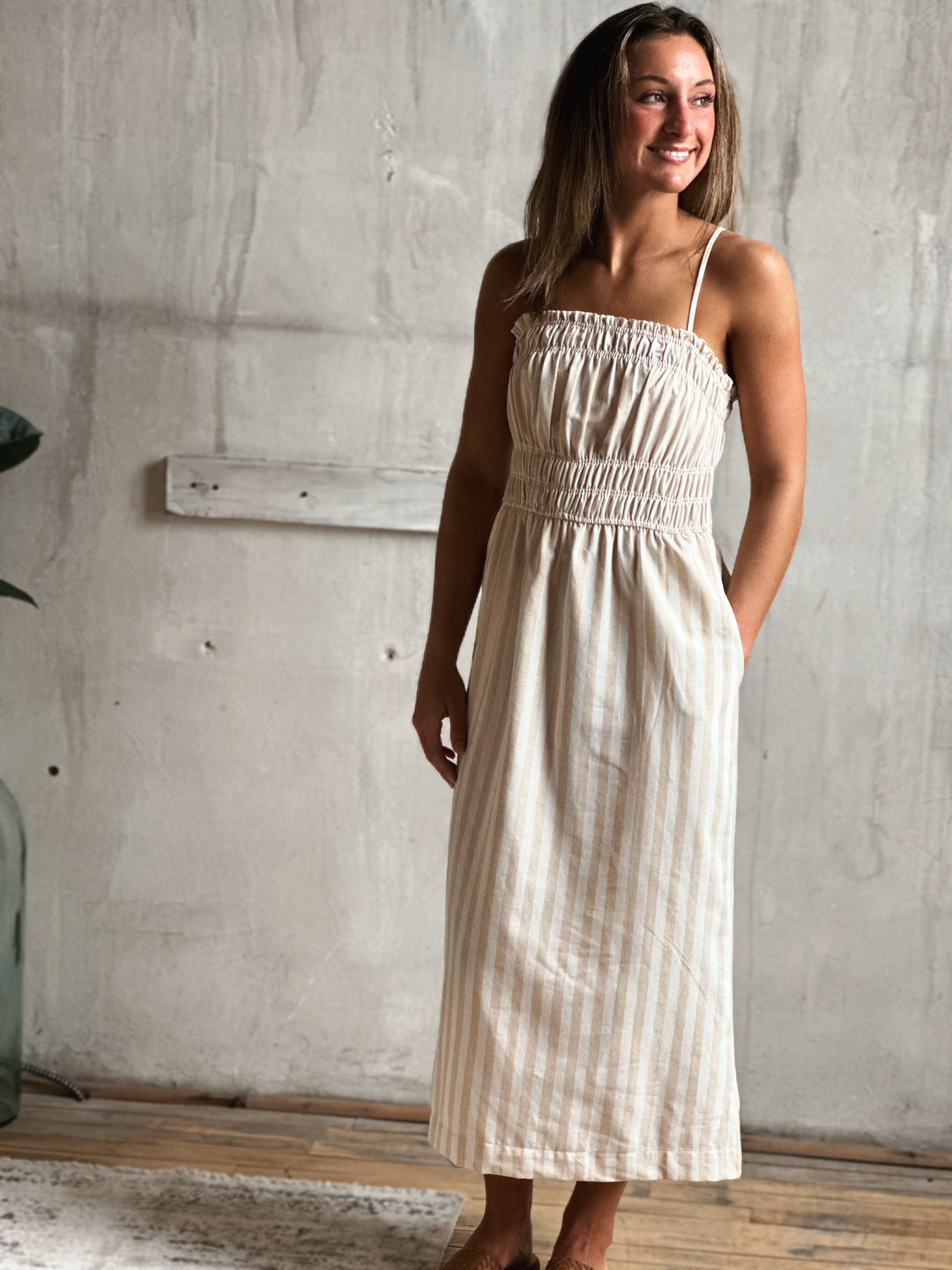 Woman wearing a white and cream striped  dress standing against a textured wall.