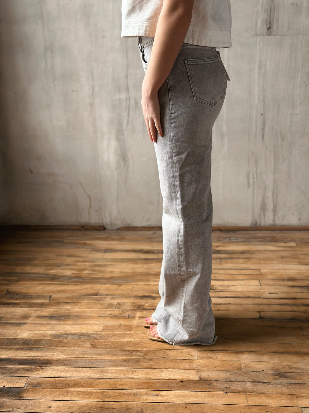 Person wearing light gray jeans standing on a wooden floor with a concrete wall background