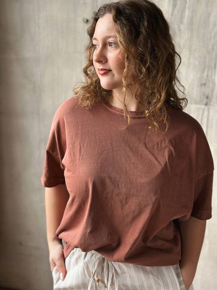 Woman wearing a brown t-shirt against a textured wall.