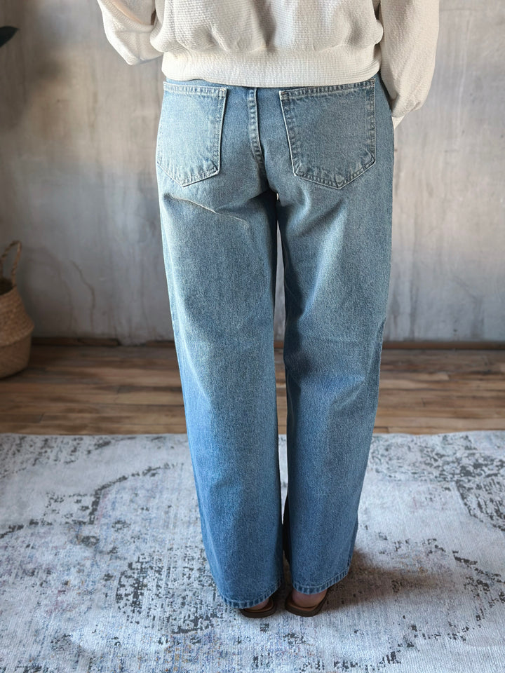 Person wearing light blue jeans standing on a textured rug with a neutral background