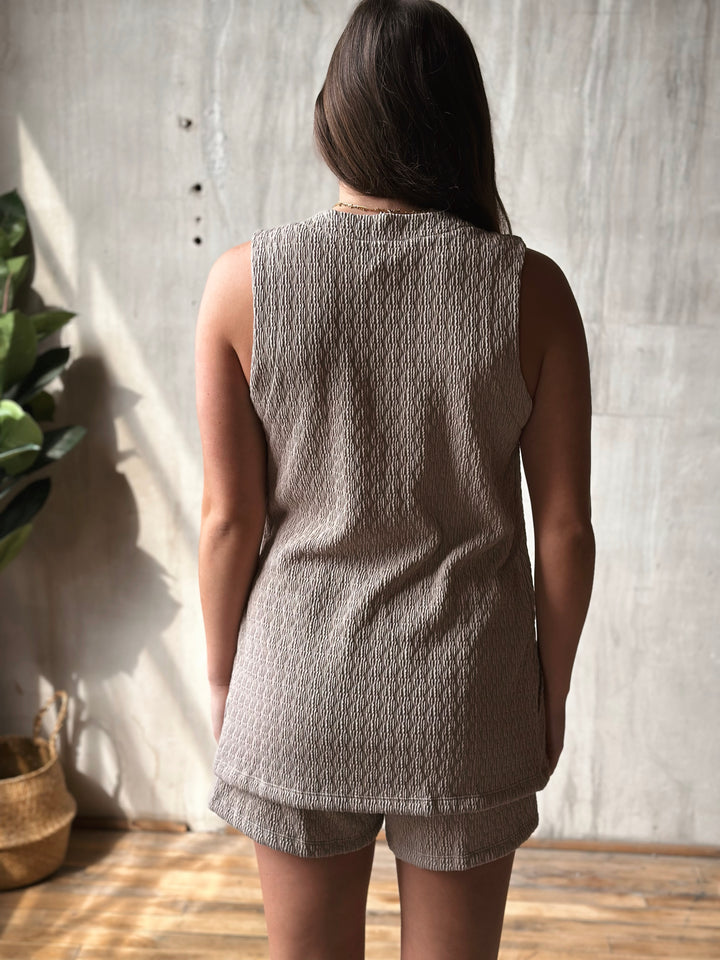 Person wearing a textured sleeveless top and shorts against a neutral wall.