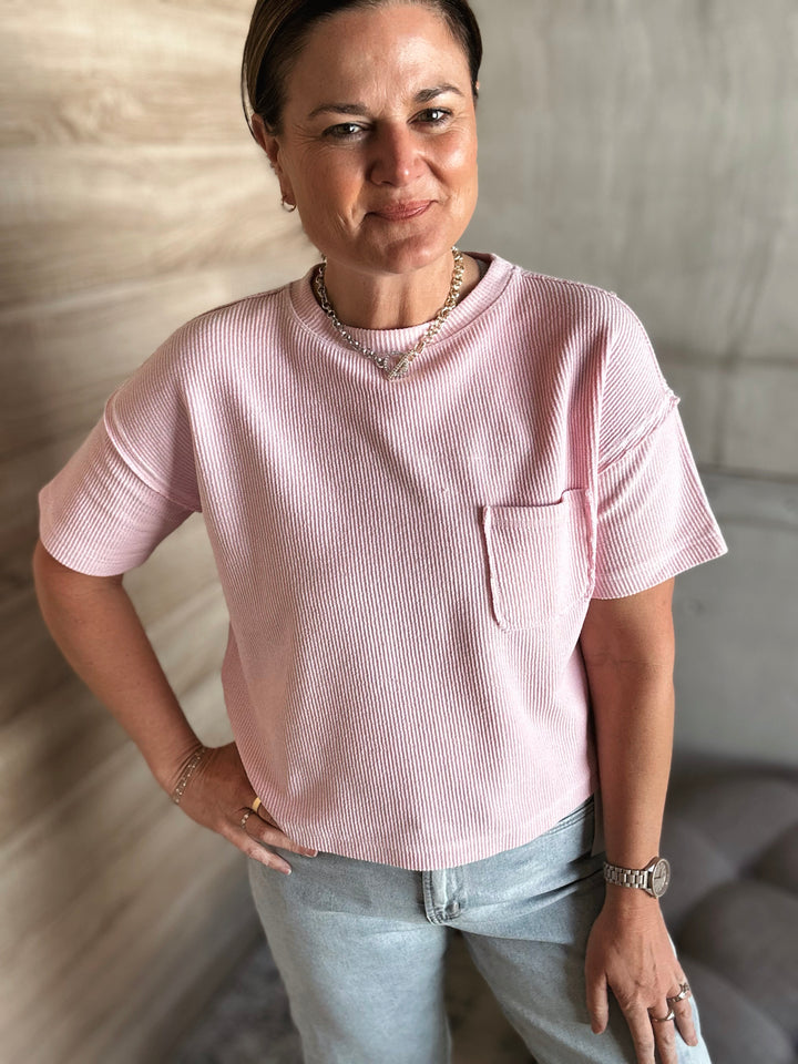 A woman wearing a textured light pink short sleeved shirt with a pocket on the left side of the shirt. 