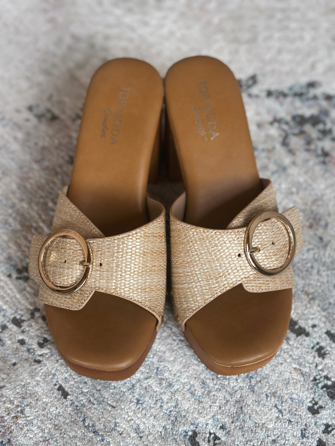 Pair of beige sandals with a large gold buckle on a textured surface.