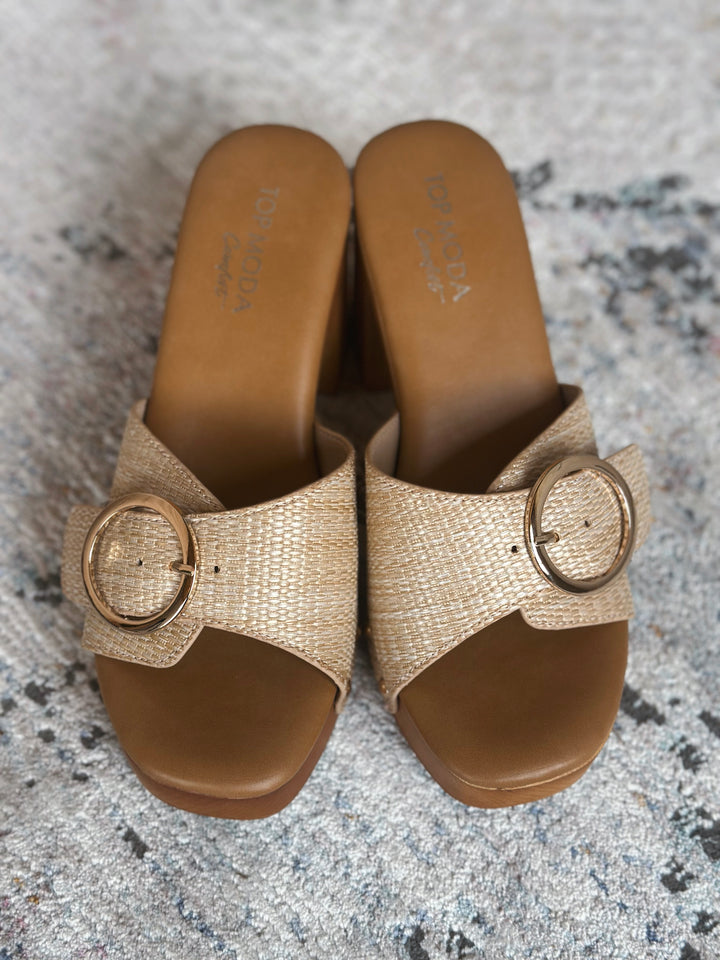 Pair of beige sandals with a large gold buckle on a textured surface.