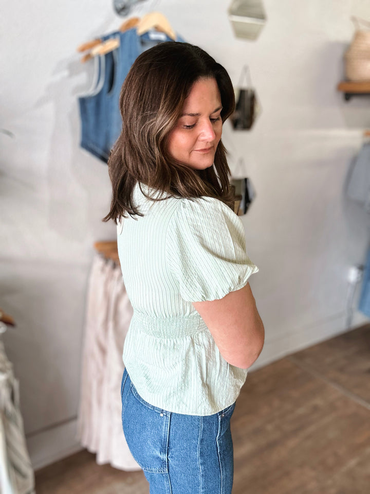 Woman wearing a light green blouse and blue jeans in a clothing store.