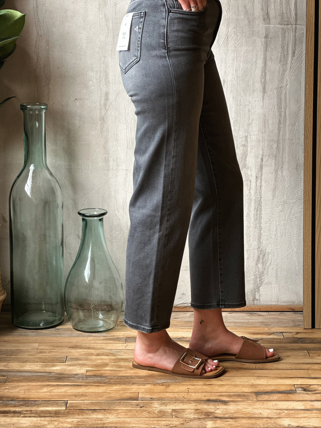 Person wearing dark jeans standing on a wooden floor with large glass bottles in the background.