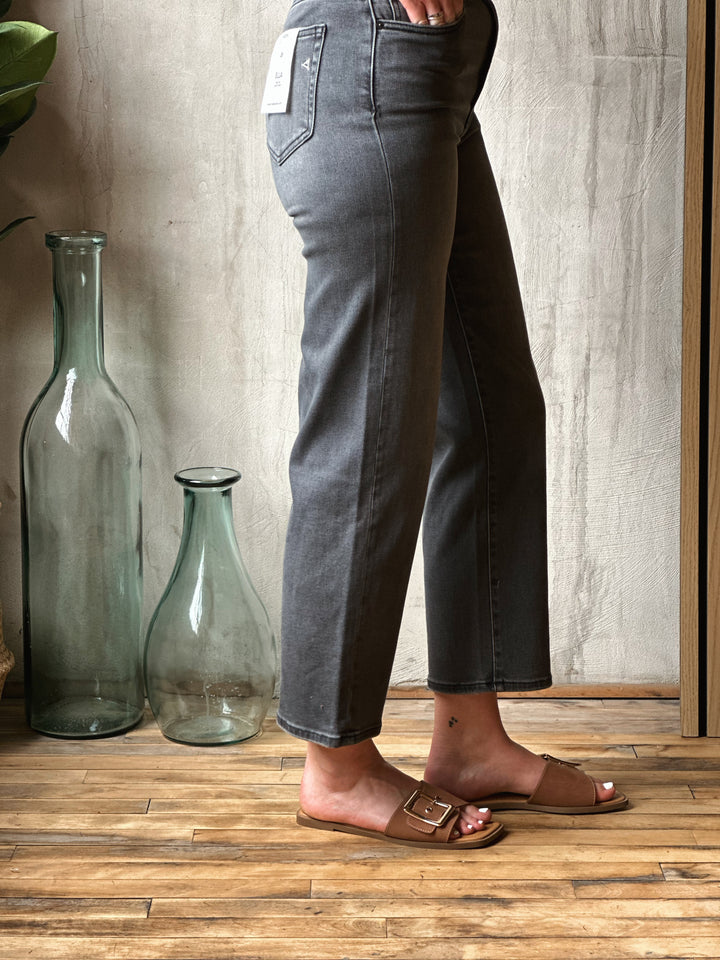 Person wearing dark jeans standing on a wooden floor with large glass bottles in the background.