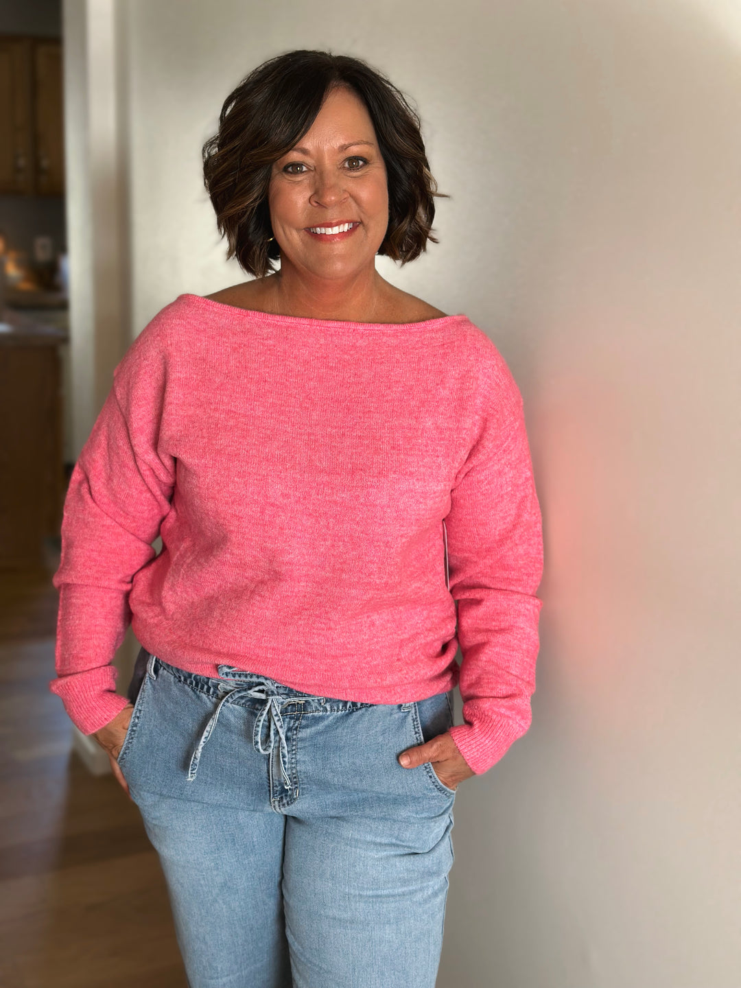 Woman wearing a pink sweater and blue jeans indoors.