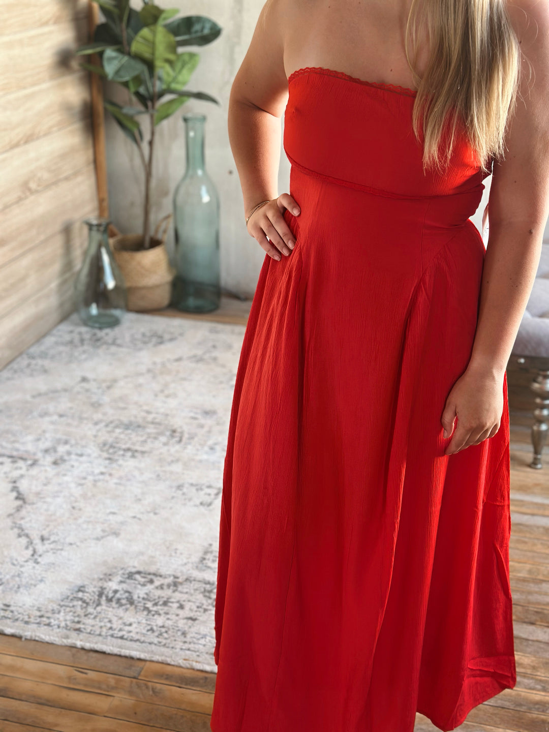 Person wearing a strapless red dress in a room with a textured rug and plant.