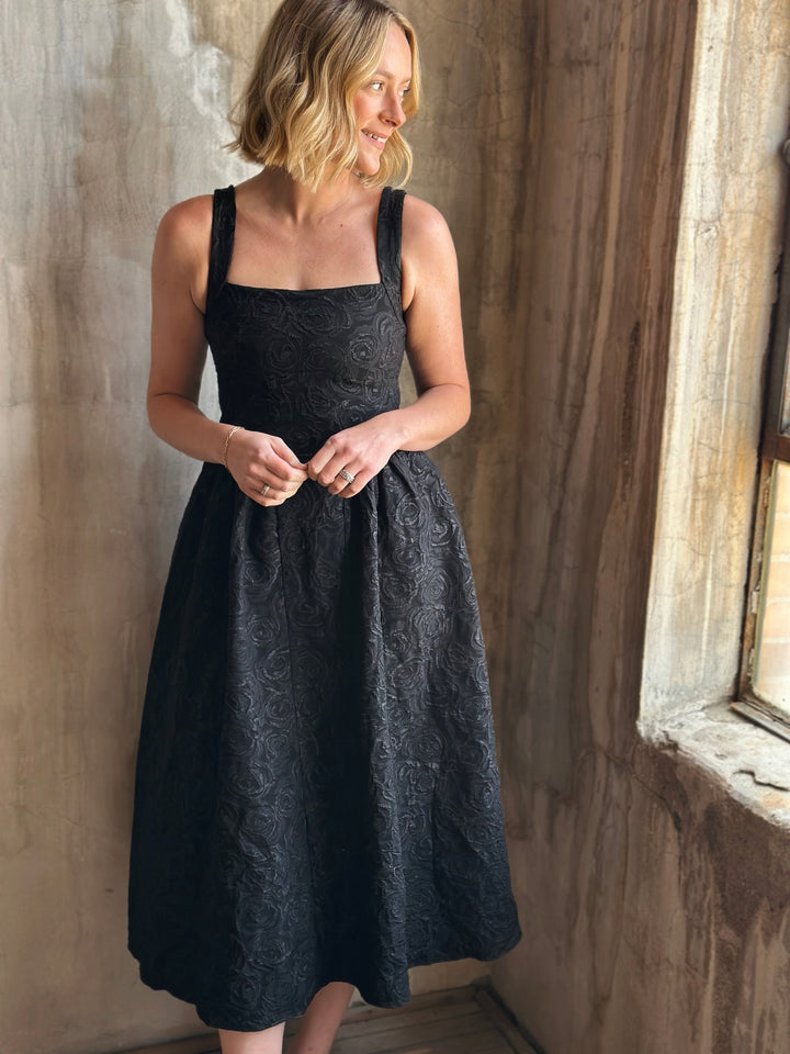 Woman wearing a black dress standing against a textured wall.