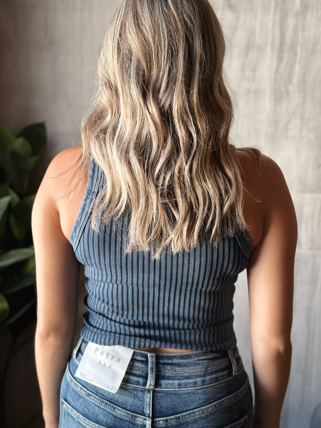 Person wearing a ribbed tank top and jeans with a neutral background