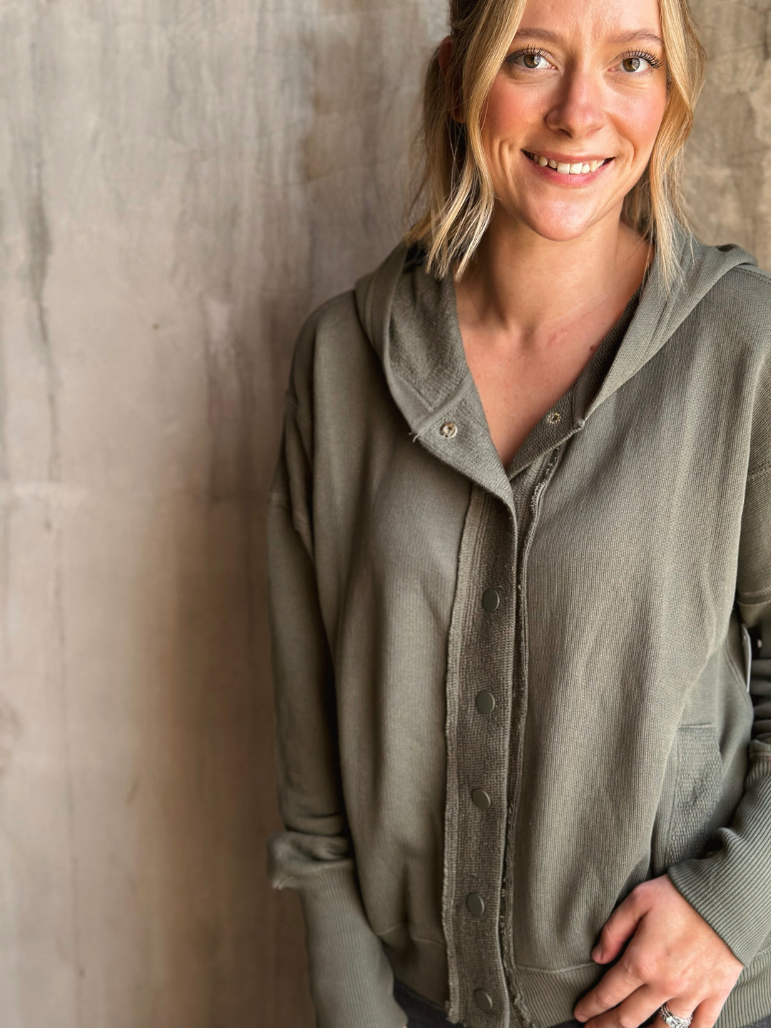 Woman wearing a green hoodie against a textured wall
