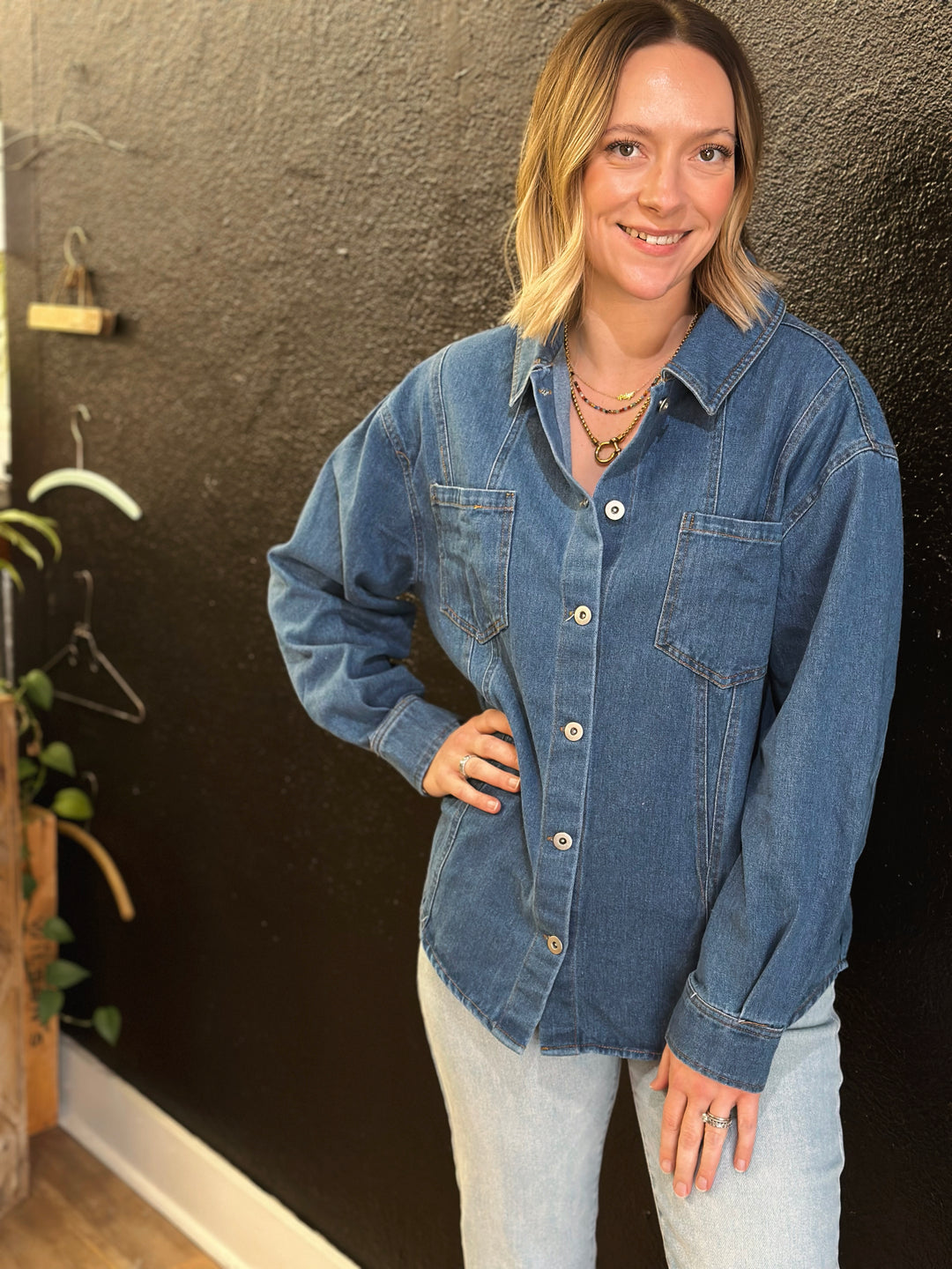 Woman wearing a denim jacket and light jeans against a dark wall.
