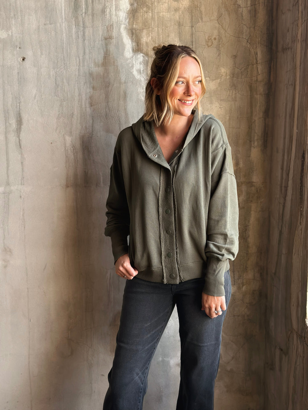 Woman wearing a green jacket and dark pants against a textured wall.