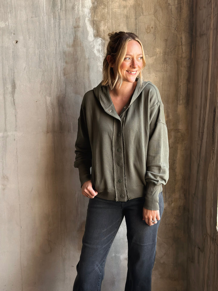 Woman wearing a green jacket and dark pants against a textured wall.