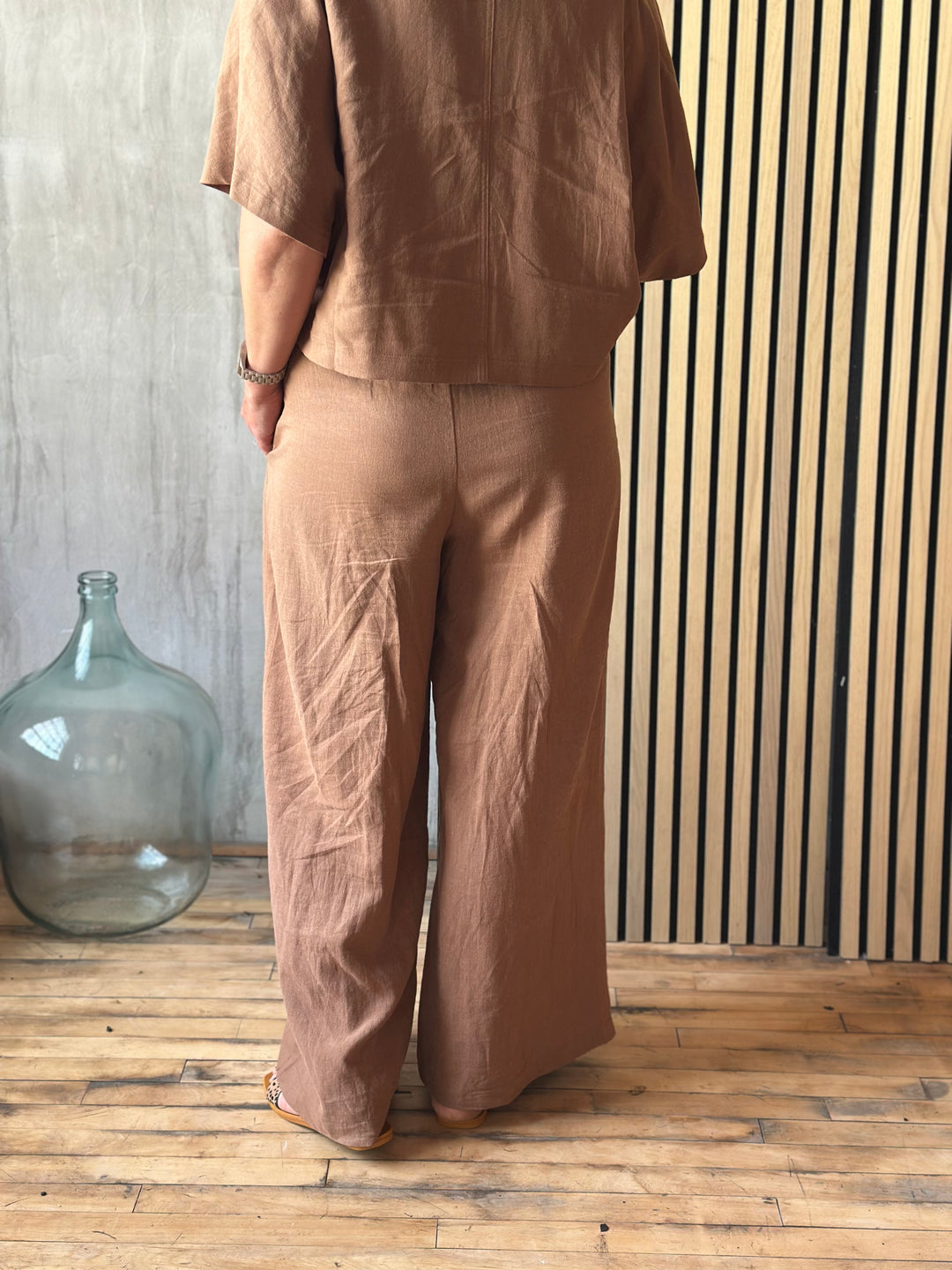 A person wearing brown pants standing against a wooden wall.