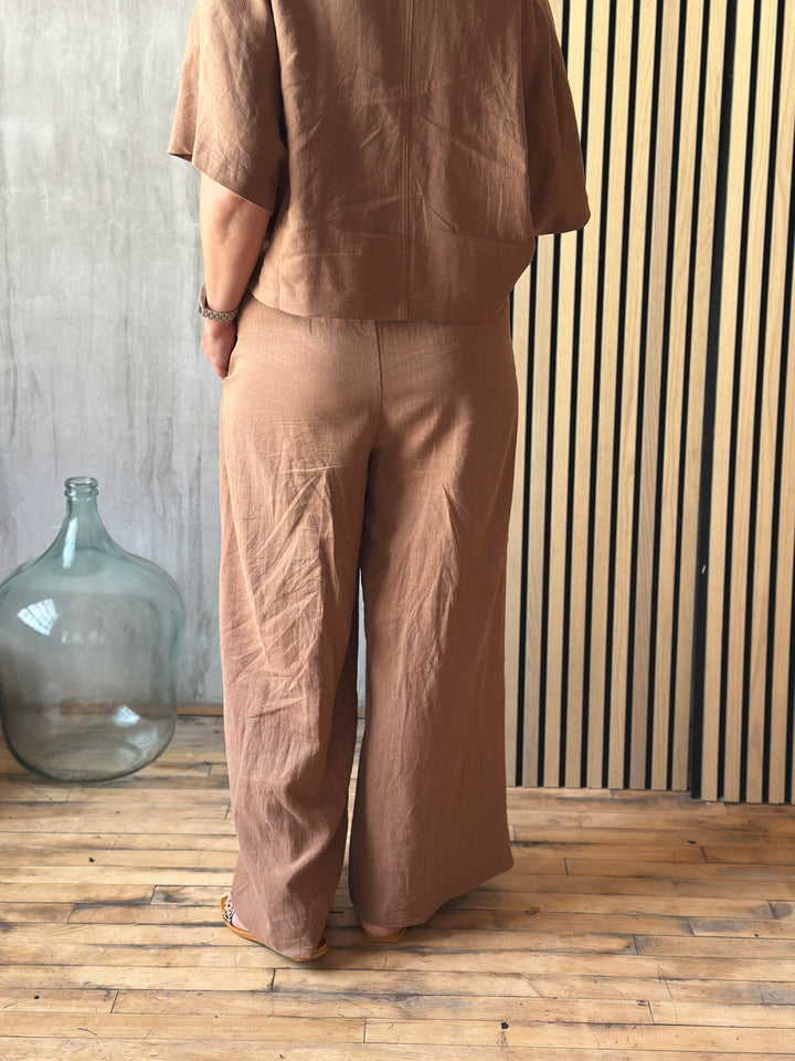 A person wearing brown pants standing against a wooden wall.
