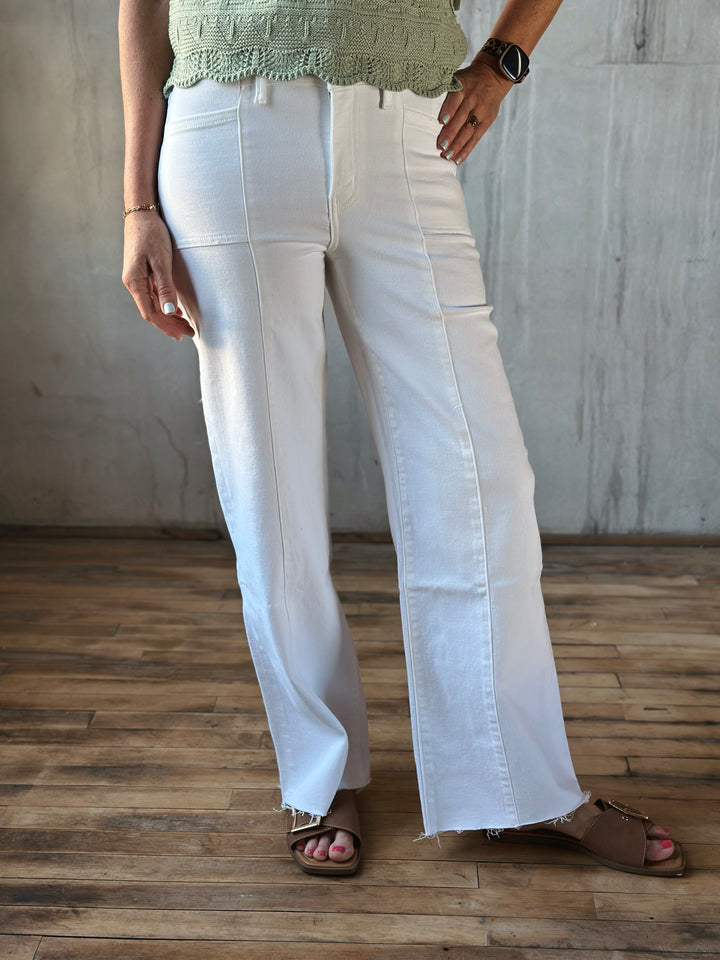 Person wearing white wide-leg pants and a green top against a plain background